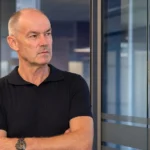 Een niet-spelende clubvertegenwoordiger in een jeugdacademie met een RSCA-embleem op een glazen wand.