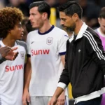 Een lid van de technische staf loopt langs spelers in witte shirts in de technische zone.