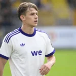 Een speler in een wit-paars Anderlecht-tenue kijkt geconcentreerd over het veld.