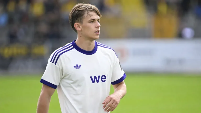 Een speler in een wit-paars Anderlecht-tenue kijkt geconcentreerd over het veld.