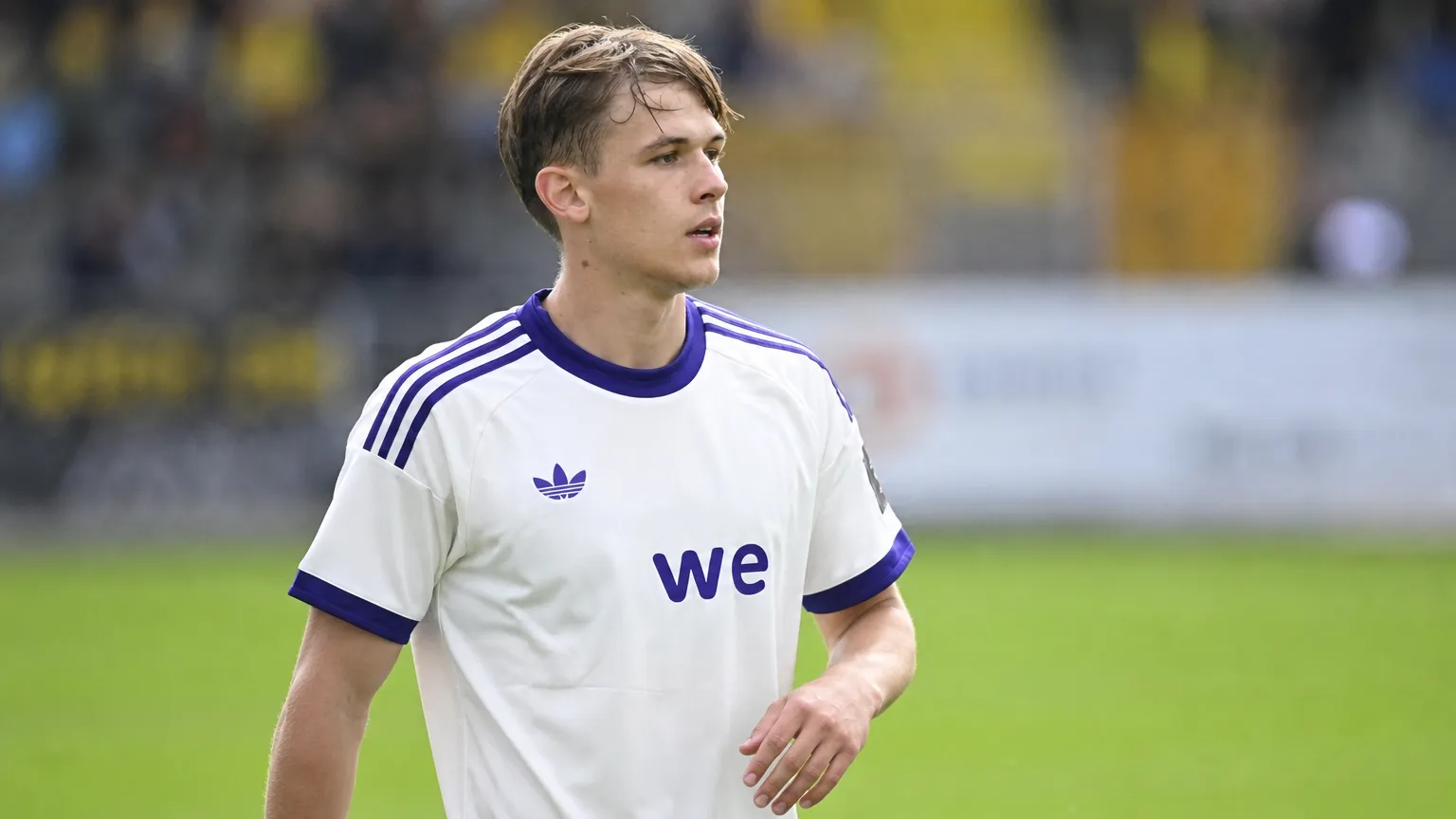 Een speler in een wit-paars Anderlecht-tenue kijkt geconcentreerd over het veld.