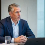 Michael Verschueren zit aan een vergadertafel in een kantoorruimte.