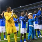 Een groep spelers van KRC Genk applaudisseert langs het veld voor de supporters.