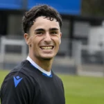 Jan Virgili staat glimlachend op een voetbalveld in een donker trainingsshirt.