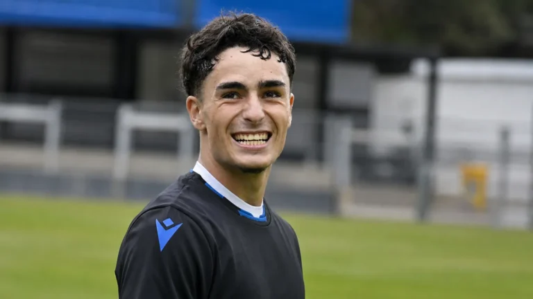 Jan Virgili staat glimlachend op een voetbalveld in een donker trainingsshirt.