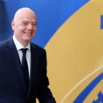 Een FIFA-official in donker pak loopt langs een blauw-gouden FIFA-decor.