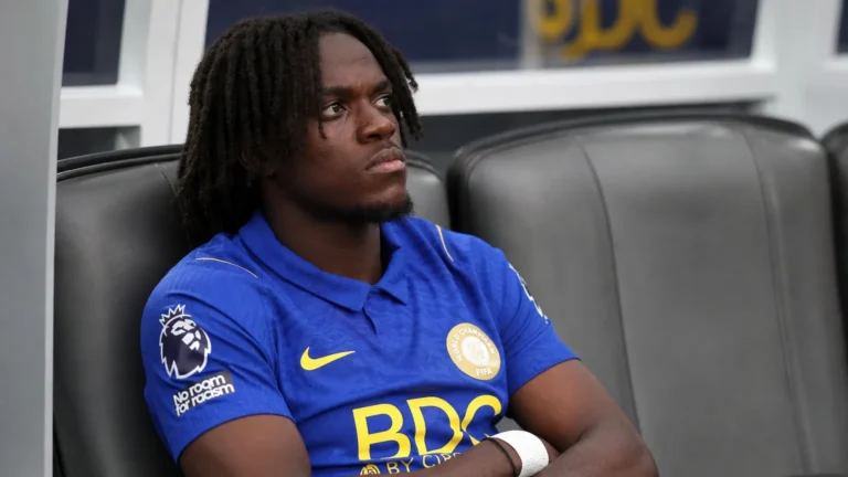 Een speler in blauw shirt zit op de spelersbank van een voetbalstadion.