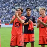 Een groep voetballers applaudisseert na een wedstrijd voor de tribunes.