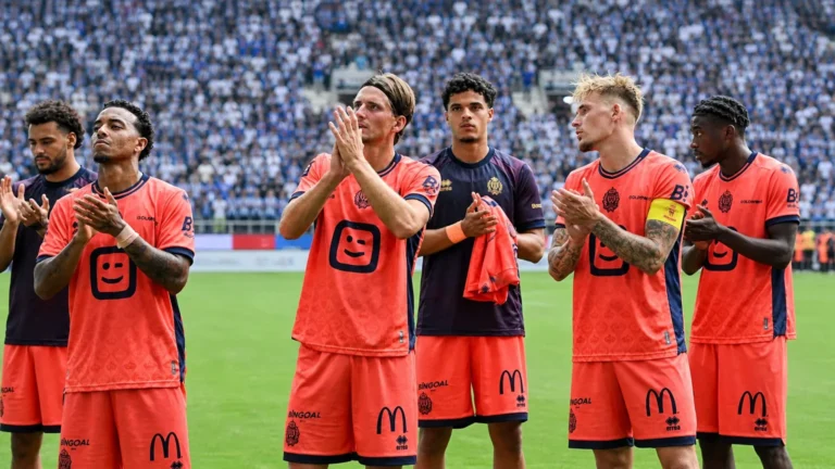 Een groep voetballers applaudisseert na een wedstrijd voor de tribunes.