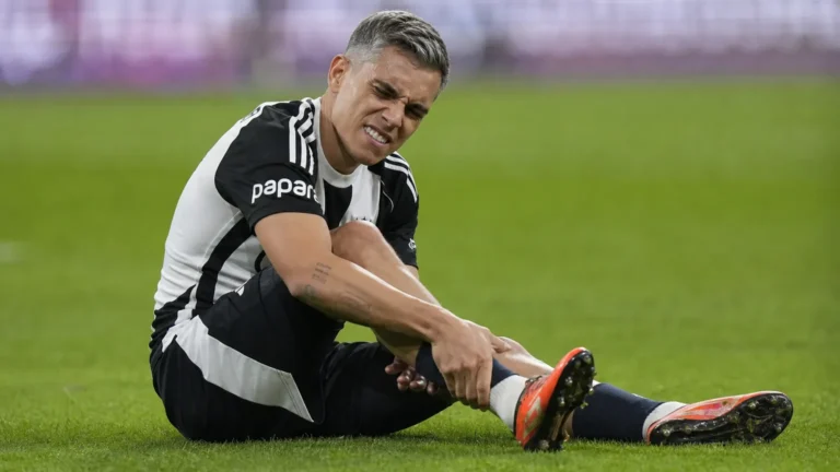 Leandro Trossard zit op het gras en houdt zijn hiel vast tijdens een wedstrijd.