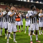 Spelers van Sporting Charleroi applaudisseren samen op het veld onder stadionlichten.