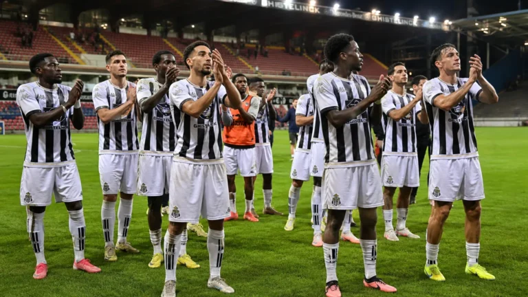 Spelers van Sporting Charleroi applaudisseren samen op het veld onder stadionlichten.