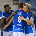 Een groep KRC Genk-spelers in blauwe wedstrijdshirts viert samen aan de zijlijn.