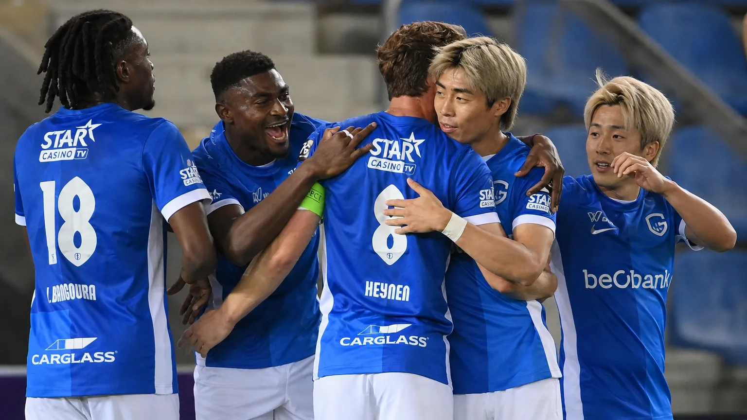 Een groep KRC Genk-spelers in blauwe wedstrijdshirts viert samen aan de zijlijn.