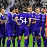 Een groep Anderlecht-spelers in paarse wedstrijdtenues verzamelt zich op het veld voor de aftrap.