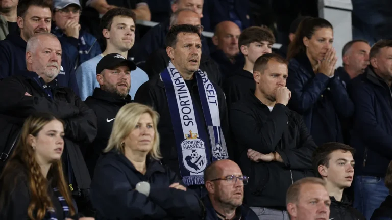 Een collectieve groep supporters van Sporting Hasselt in de tribune met een club-sjaal.