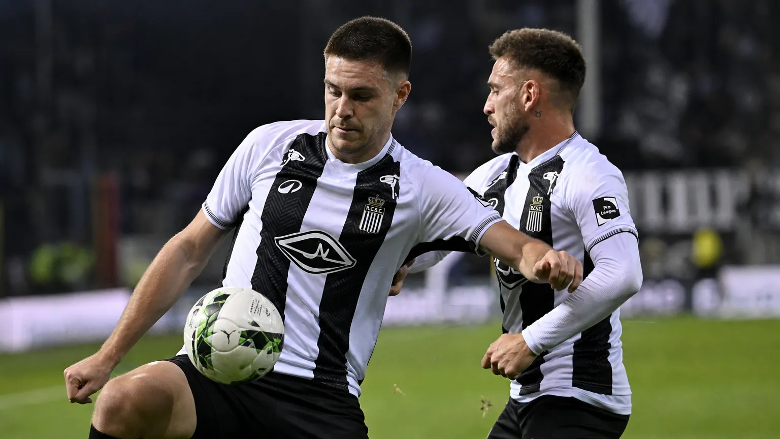 Twee spelers in zwart-witte shirts tijdens een wedstrijdmoment op het veld.