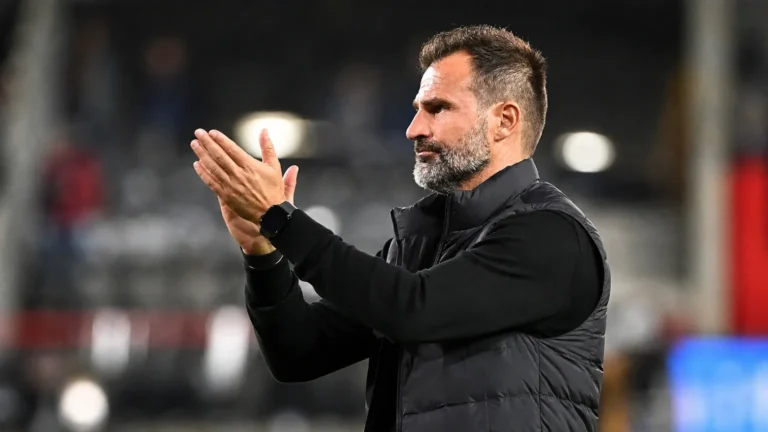 Een coach van Club Brugge applaudisseert langs de zijlijn in een stadion.