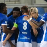 Een groep voetballers in blauwe shirts viert samen tijdens een wedstrijdmoment.