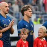 Een groep Antwerp-spelers in blauwe wedstrijdshirts staat met jonge begeleiders klaar voor een competitiewedstrijd.