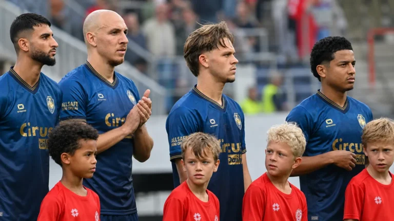 Een groep Antwerp-spelers in blauwe wedstrijdshirts staat met jonge begeleiders klaar voor een competitiewedstrijd.