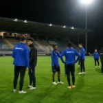 Een groep spelers in blauwe sportkleding tijdens een rustig moment op het veld van Den Dreef.