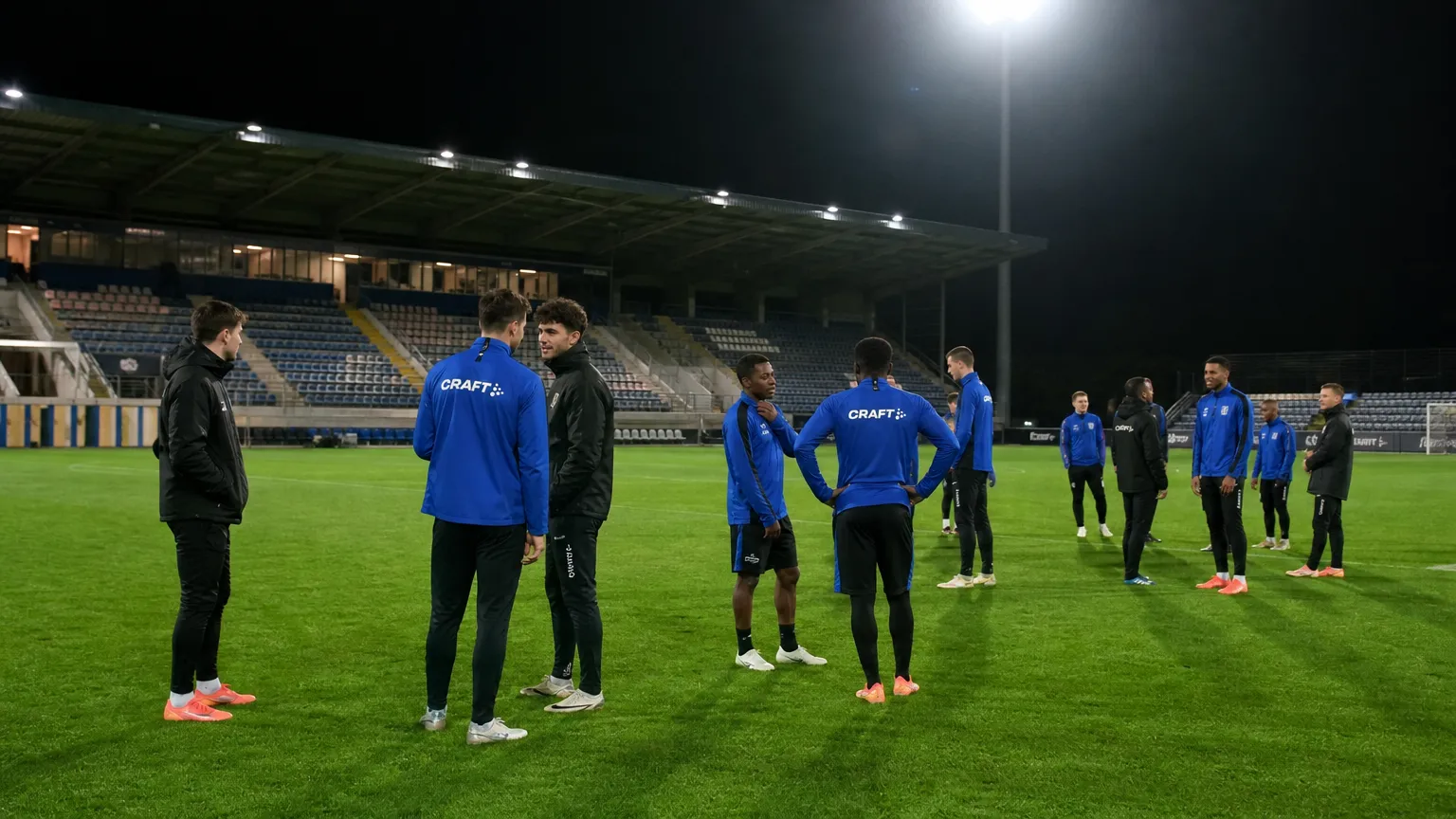 Een groep spelers in blauwe sportkleding tijdens een rustig moment op het veld van Den Dreef.
