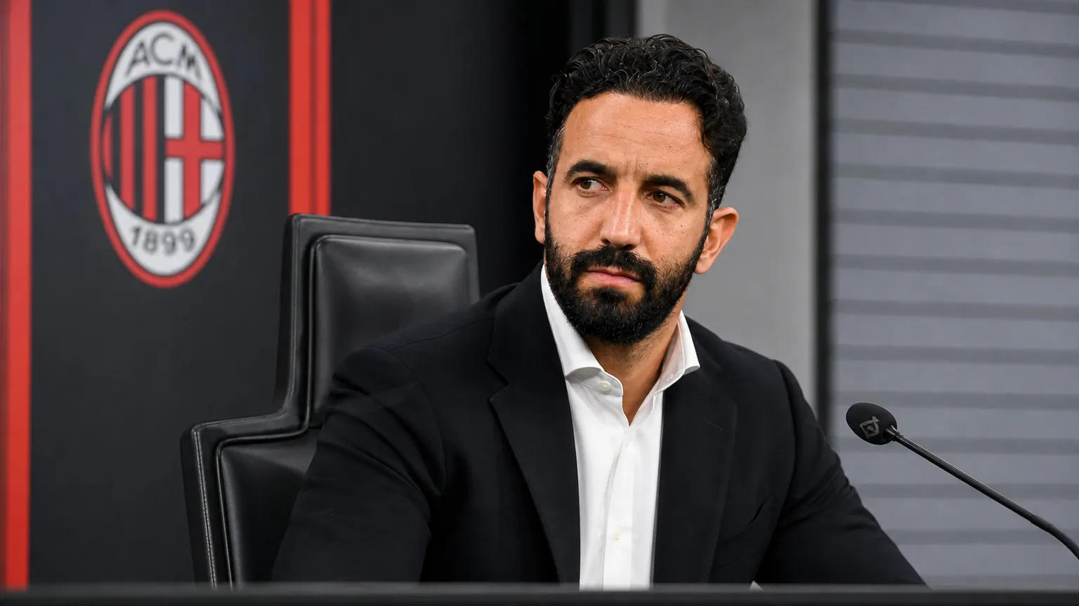Rúben Amorim in zwart pak tijdens een persconferentie van AC Milan.