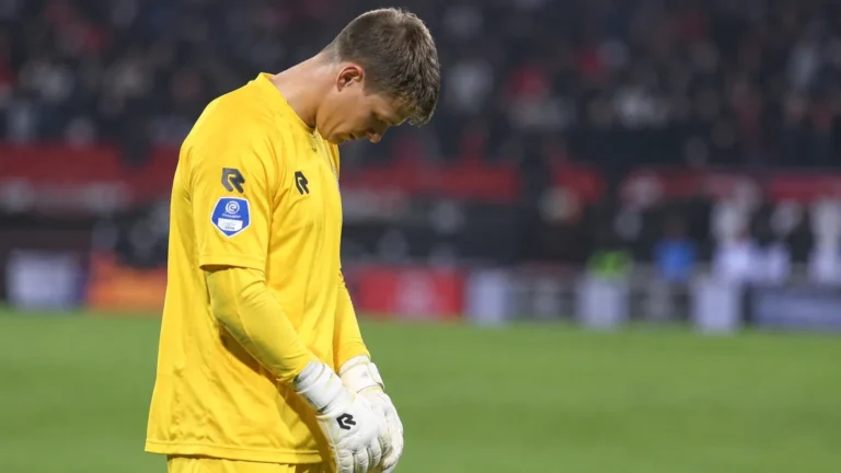 Een doelman in geel staat met gebogen hoofd op het veld tijdens een steunbetuiging.