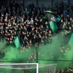 Een volle groep Cercle Brugge-supporters met groen-zwarte vlaggen in de tribune.