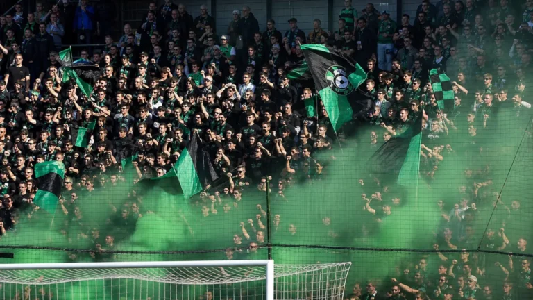 Een volle groep Cercle Brugge-supporters met groen-zwarte vlaggen in de tribune.