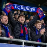 Een collectieve groep FC Dender-supporters viert in de tribune met een blauw-rode sjaal.
