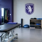Lege revalidatieruimte met enkeltrainingsmateriaal en een Beerschot-embleem op de achterwand.
