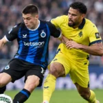 Twee voetballers in blauw-zwart en geel vechten een duel uit op het veld.