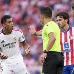 Scheidsrechter toont een kaart tijdens een derbyfase met spelers van Real Madrid en Atlético Madrid.