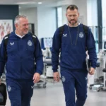 Twee medewerkers in donkere clubtrainingspakken in een medische behandelruimte.