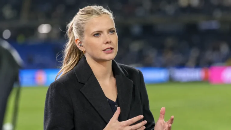 Noa Vahle tijdens een voetbaluitzending met een oortje en donkere blazer.