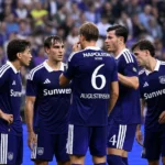 Een groep Anderlecht-spelers in paarse wedstrijdtenues overlegt tijdens een spelonderbreking.