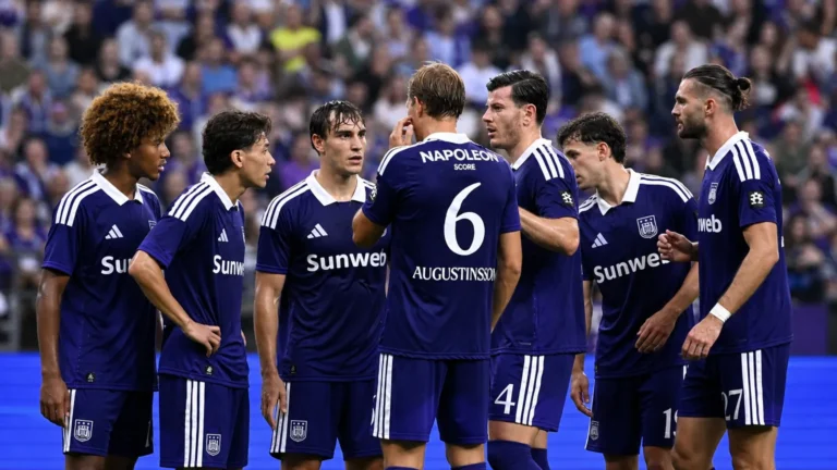 Een groep Anderlecht-spelers in paarse wedstrijdtenues overlegt tijdens een spelonderbreking.