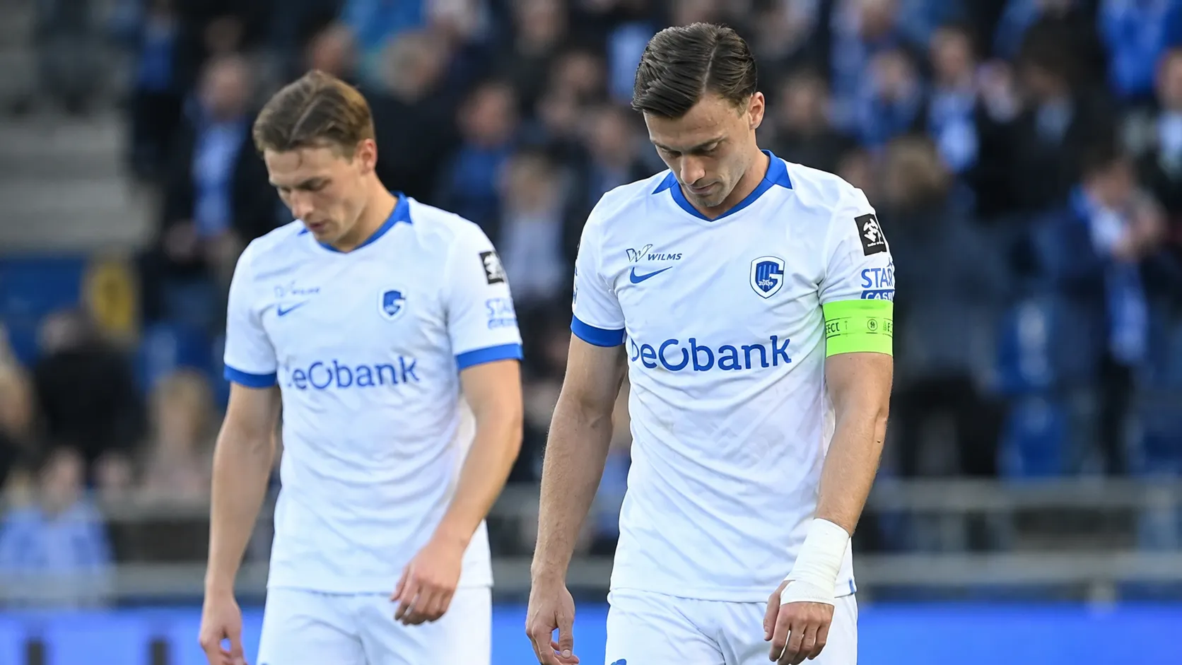 Twee spelers in witte shirts lopen na afloop over het veld.