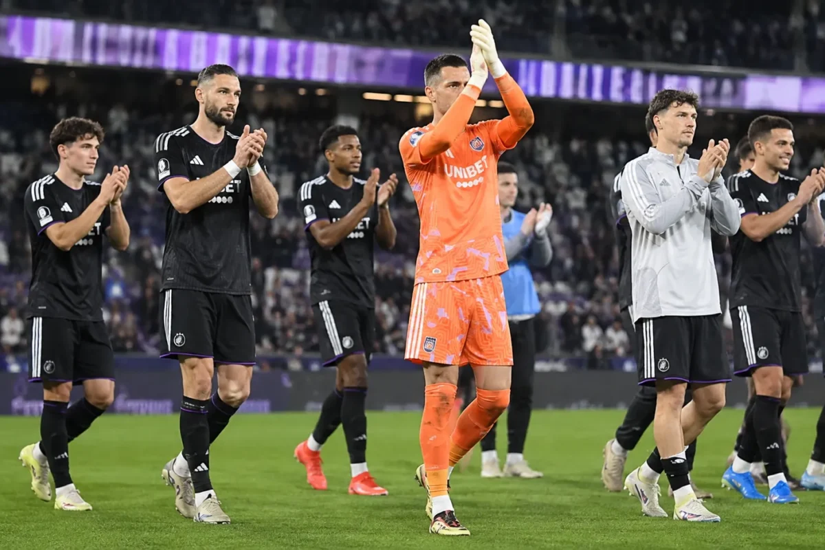 Een groep voetballers, onder wie een doelman in oranje, applaudisseert op het veld.