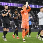 Een groep voetballers, onder wie een doelman in oranje, applaudisseert op het veld.