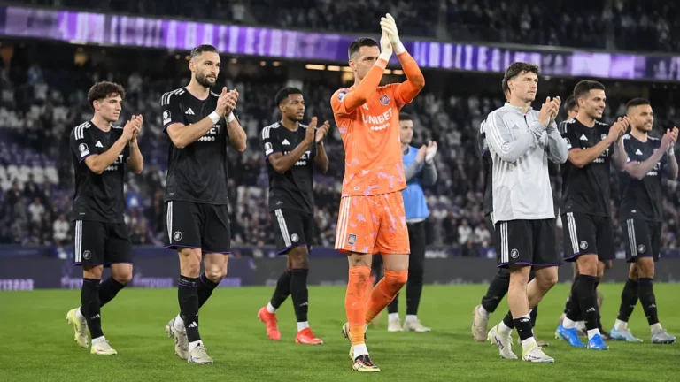Een groep voetballers, onder wie een doelman in oranje, applaudisseert op het veld.