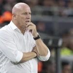 Fred Vanderbiest in een wit hemd langs de zijlijn van een voetbalstadion.