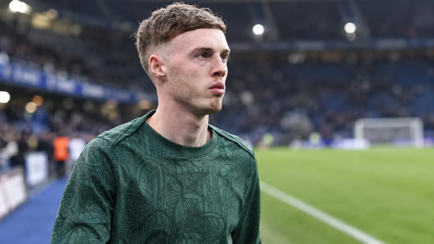 Cole Palmer in een groen Chelsea-warm-upshirt naast het veld.