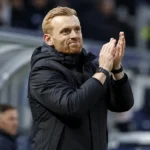 Edward Still applaudisseert vanuit de technische zone tijdens een voetbalwedstrijd.