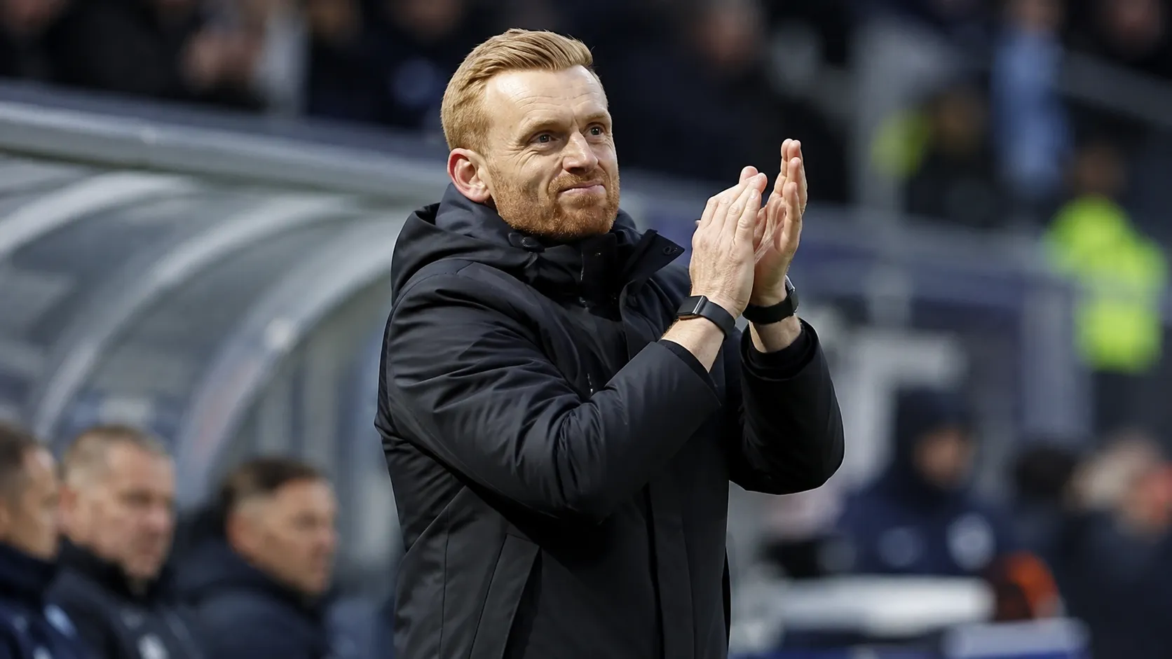 Edward Still applaudisseert vanuit de technische zone tijdens een voetbalwedstrijd.