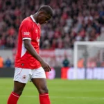Een Antwerp-speler in rood-wit wandelt op het veld na een wedstrijdmoment.