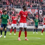 Voetballers in rode en groen-zwarte tenues tijdens een onderbreking op het veld.
