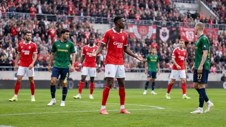 Voetballers in rode en groen-zwarte tenues tijdens een onderbreking op het veld.